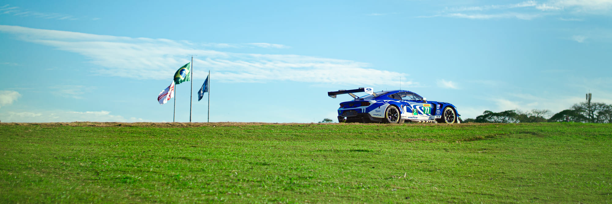 Ford Mustang GT3 #77 da Proton Competition, da classe LMGT3, recortado na linha do horizonte ao lado das bandeiras do Brasil e de São Paulo, com Eric Powell, Ben Tuck e Sebastian Priaulx, no WEC 6 Horas de São Paulo 2026, em Interlagos