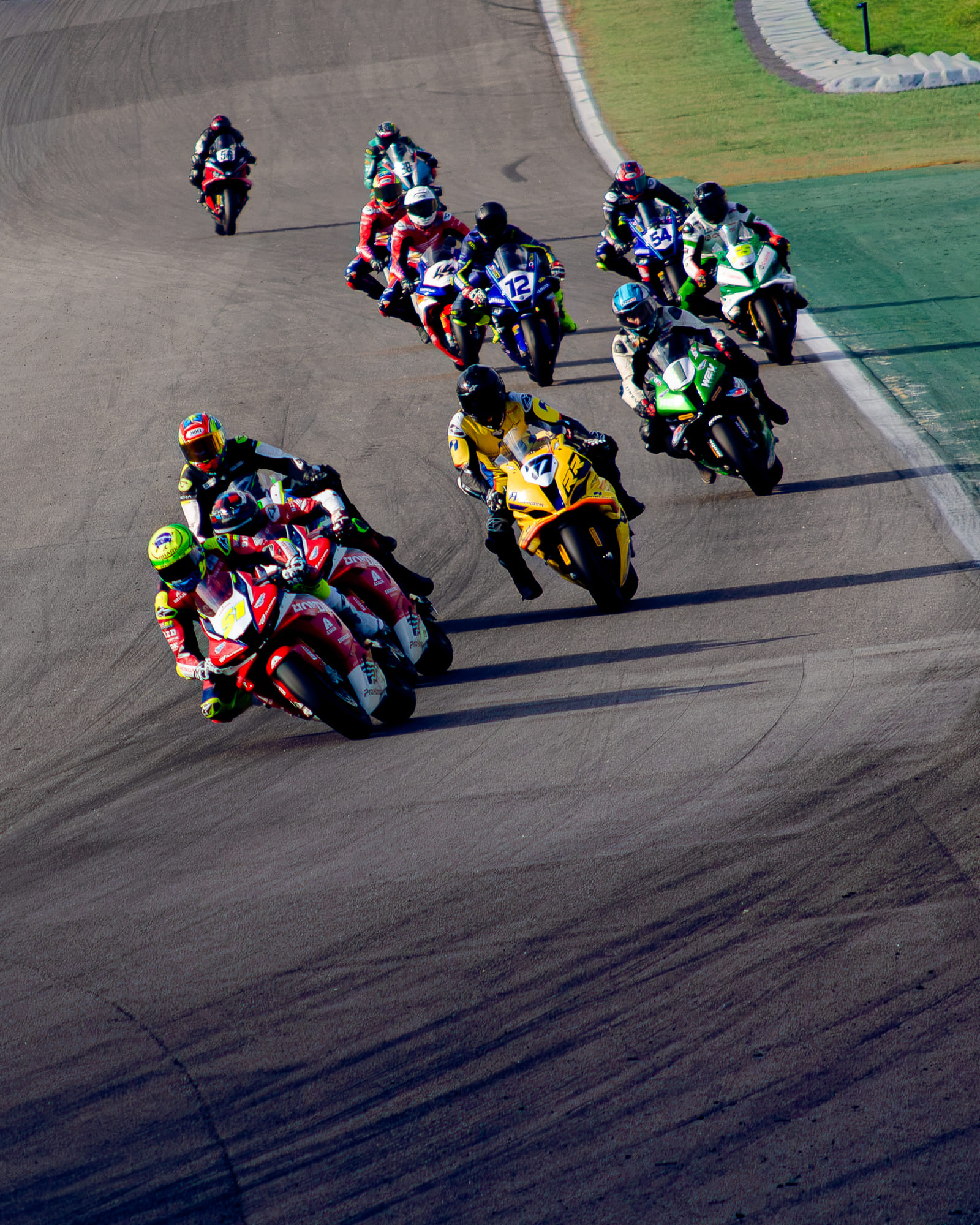 Pelotão de superbikes da classe GP1000 mergulhando na curva sob luz baixa, com a Honda #51 na frente, na Moto1000GP 2026 - Etapa 5, em Interlagos