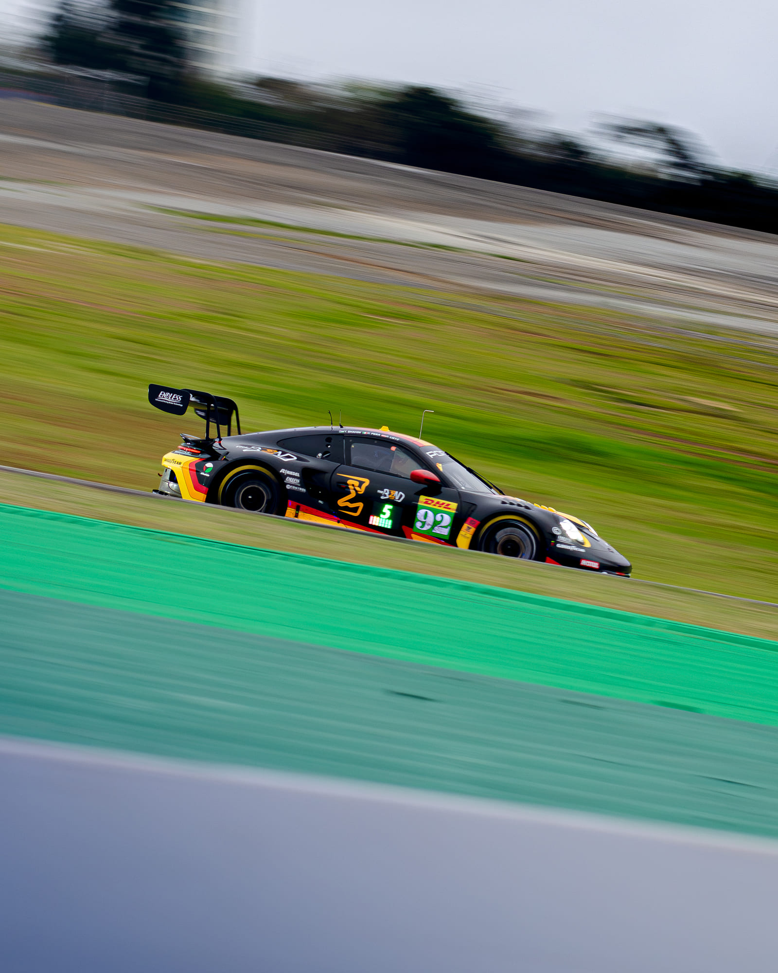 Porsche 911 GT3 R #92 preto e laranja da The Bend Manthey, da classe LMGT3, em velocidade com o fundo varrido pelo panning, pilotado por Yasser Shahin, Riccardo Pera e Richard Lietz no WEC 6 Horas de São Paulo 2026, em Interlagos