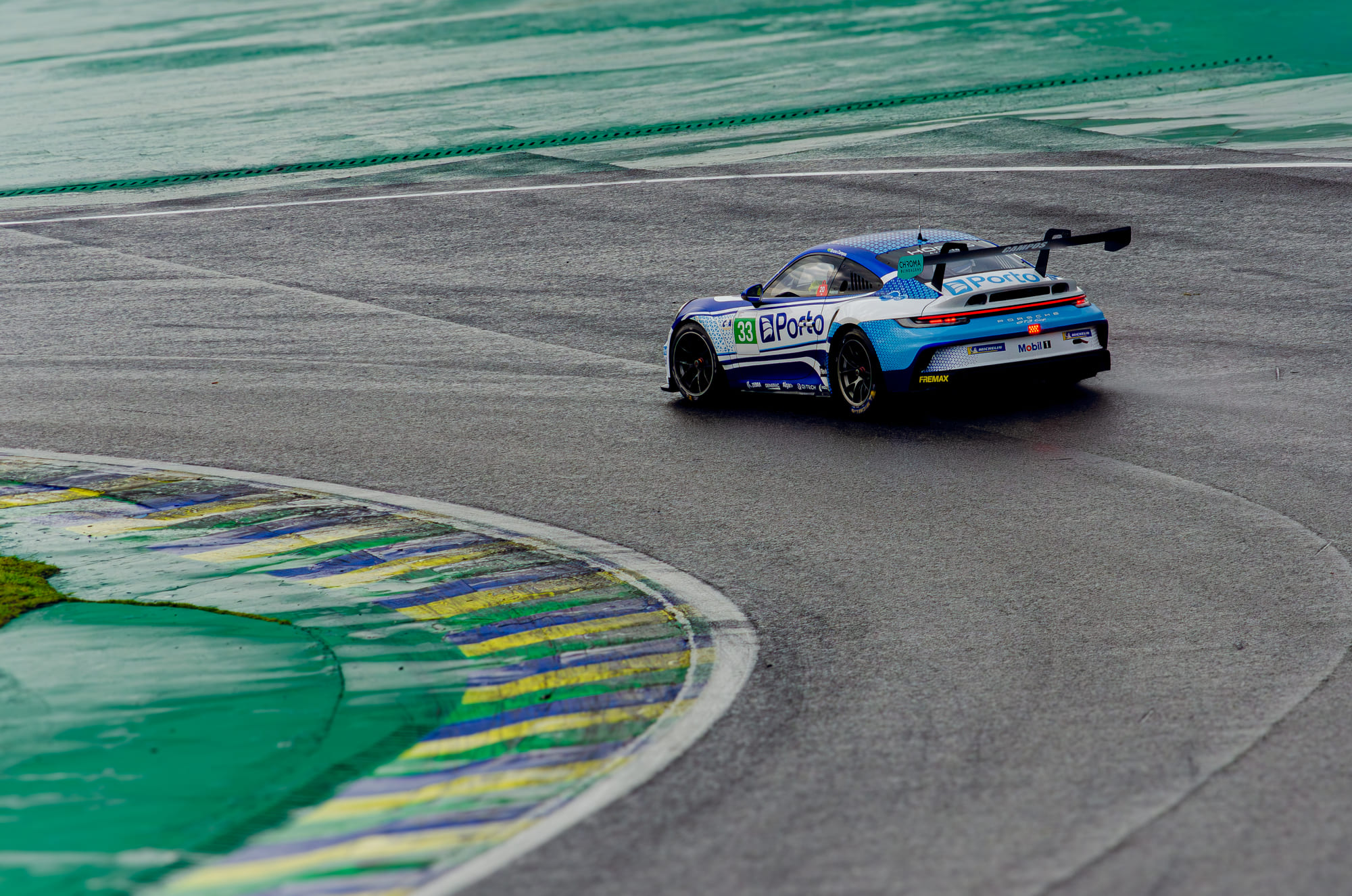 Porsche 911 GT3 Cup #33 da Porto Seguro, da classe Carrera Rookie, cruzando o asfalto molhado, visto de traseira, com Bruno Campos ao volante na Porsche Cup Brasil 2026 - Etapa 7, em Interlagos
